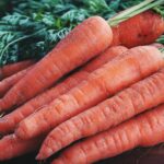 Close-up of fresh organic carrots with greens on a wooden surface, showcasing vibrant orange color.