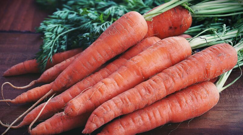 Close-up of fresh organic carrots with greens on a wooden surface, showcasing vibrant orange color.