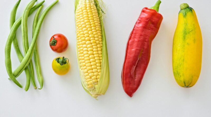 A vibrant assortment of fresh vegetables including corn, peppers, beans, and tomatoes.