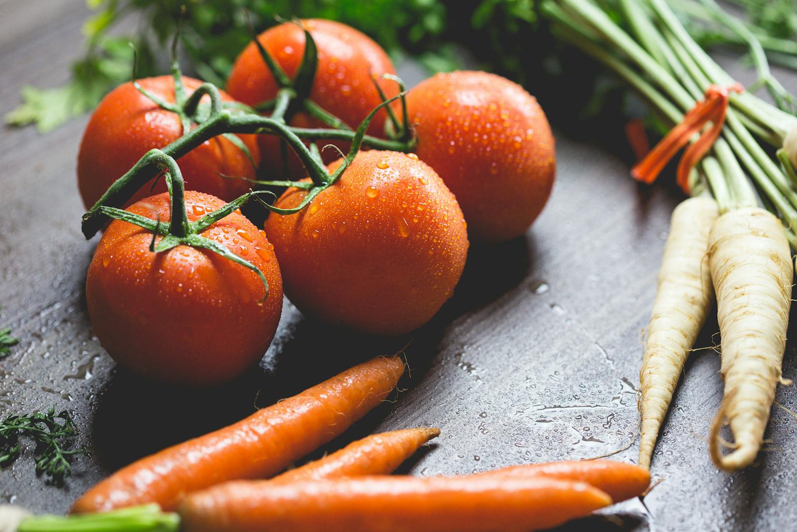 Close-up of fresh tomatoes and carrots with water droplets on a wooden surface.