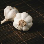 Two fresh garlic bulbs on a dark wooden mat, highlighting aromatic culinary ingredients.