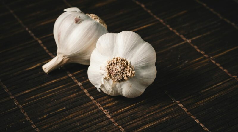 Two fresh garlic bulbs on a dark wooden mat, highlighting aromatic culinary ingredients.